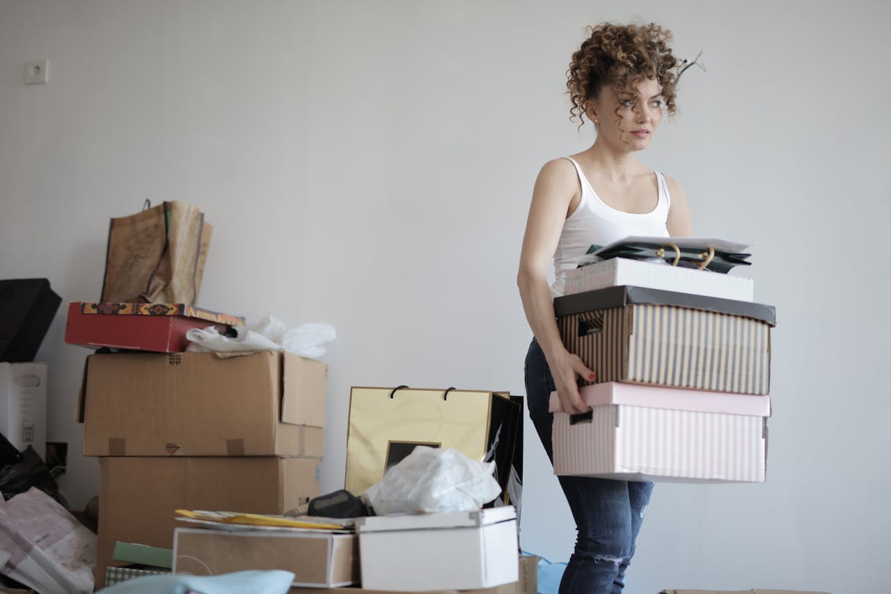 portfolio-05 A young woman carrying boxes during a move into a new apartment, surrounded by packed belongings.