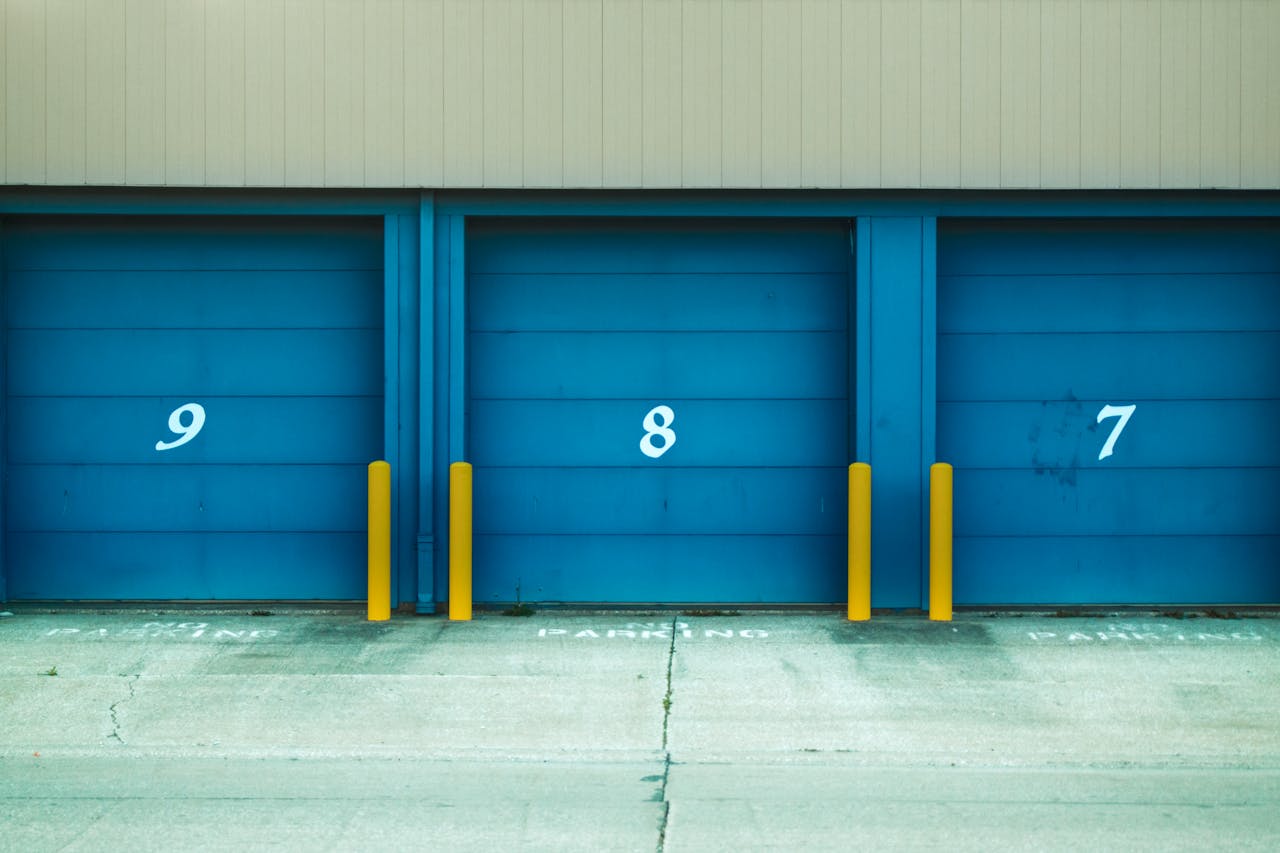 portfolio-03 Three blue shutter doors numbered 9, 8, and 7 with yellow barriers in urban environment.